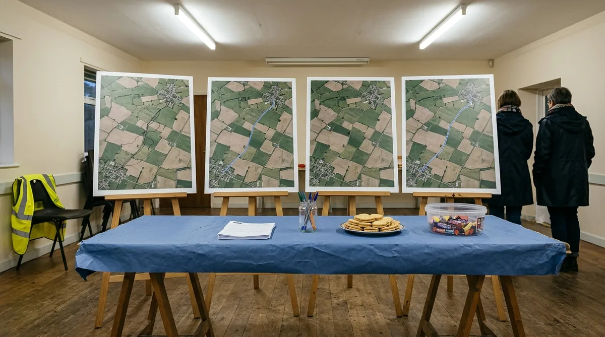 A village hall trestle table at an evening drop-in consultation, covered in a blue paper cloth